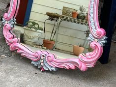 a pink and silver mirror sitting on the ground next to a building with potted plants