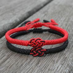 two red and black bracelets sitting on top of a wooden table