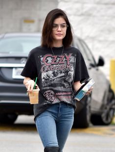 a woman walking down the street wearing glasses and holding a coffee cup in her hand