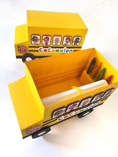 a school bus shaped box with pens and crayons in the bottom section, sitting on a white surface