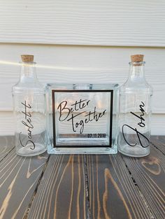 two glass bottles sitting on top of a wooden table next to each other with writing on them