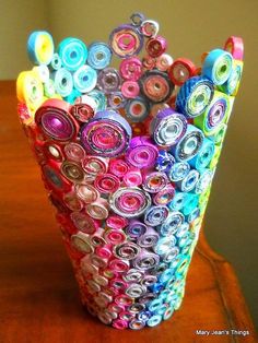 a vase filled with lots of different colored rolled up paper circles on top of a wooden table