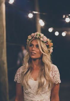 a woman wearing a flower crown standing in front of some lights and looking off to the side