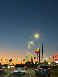 cars driving down the road at night with traffic lights and mcdonald's signs in the background