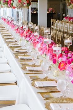 the long table is set with white chairs and pink flowers on each chair, along with gold place settings