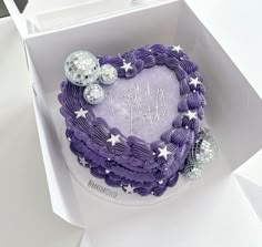 a purple heart shaped cake in a box with silver decorations on the top and bottom