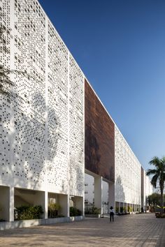 the building is made up of white perfored panels and has two people walking by it