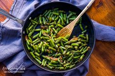 a skillet filled with green beans on top of a blue cloth and wooden spoon