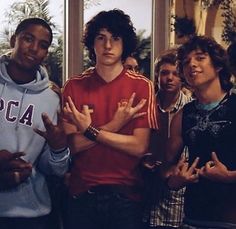 four young men standing in front of a window with their hands up to the side