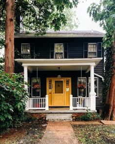 a yellow door sits in front of a black house with white pillars and columns on the porch