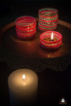 three lit candles sitting on top of a metal tray next to a candle holder filled with glass beads