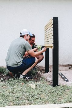 two men working on a wooden structure in the grass next to a wall and fence