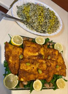 two plates of food on a table with lemons, rice and other foods next to it