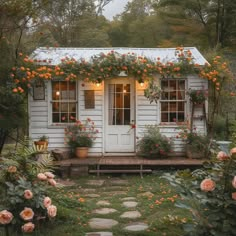 a small white house with orange flowers growing on it's roof and windows above the door