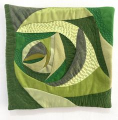 a green and white quilted wall hanging on the side of a wall with an abstract design