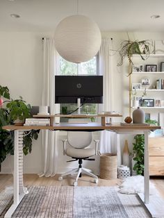 a desk with a computer on it in front of a window and potted plants