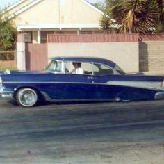 an old car is parked on the street in front of a brick wall and palm trees