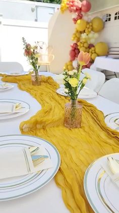 the table is set with white plates and yellow napkins, flowers in vases