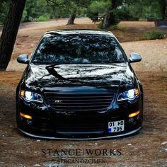 the front end of a black car parked on a dirt road next to some trees