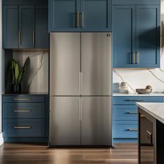 a stainless steel refrigerator in a kitchen with blue cabinets and wood flooring on the walls