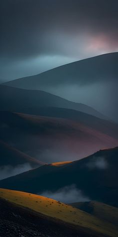 the hills are covered in fog and light at night, with low lying clouds above them