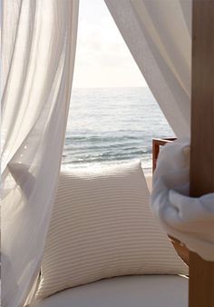 a bed sitting on top of a sandy beach next to the ocean under a canopy