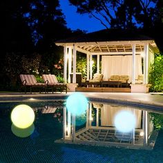 a gazebo sitting next to a swimming pool at night with lights on the ground