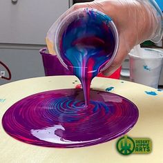 a person is pouring blue and purple paint on a table