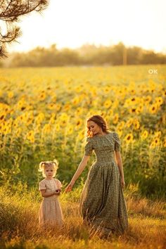 a mother and daughter holding hands while walking through a field of sunflowers at sunset