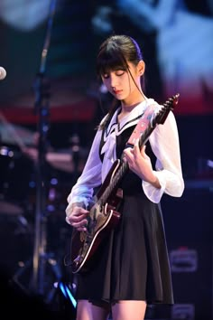 a girl in a short black dress playing an electric guitar and singing into a microphone