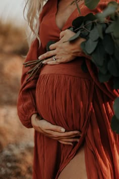 a pregnant woman in an orange dress is holding her belly with greenery on it