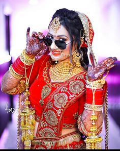 a woman in a red and gold bridal outfit holding her hands up to her face