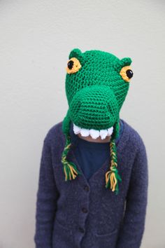 a crocheted alligator head with yellow eyes and green hair, wearing a blue cardigan