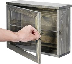 a hand is opening the door to a wooden cabinet with glass shelves on both sides