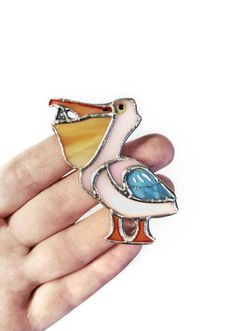 a hand holding a colorful bird brooch in it's right hand and wearing a ring