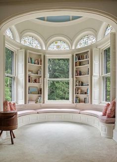 an arched window in the corner of a room with a bench and bookshelf