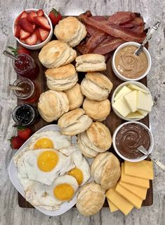 an assortment of breakfast foods laid out on a cutting board with eggs, biscuits and fruit