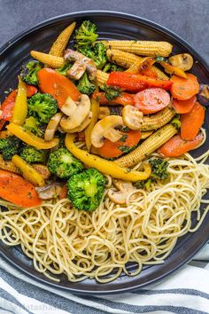 a black plate topped with pasta and veggies on top of a blue table cloth