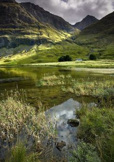 there is a small lake in the middle of some mountains with grass growing on it