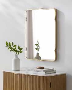 a white vase sitting on top of a wooden dresser next to a mirror and plant