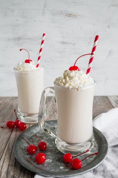 two glasses filled with whipped cream and cherries on a plate next to each other