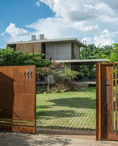 an open gate leading to a house in the middle of a yard with trees and bushes