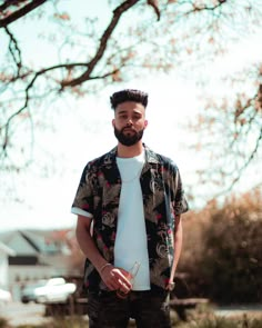 a man standing in front of a tree with his hands in his pockets and looking at the camera