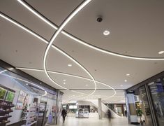 the interior of a shopping mall with white lights on the ceiling and people walking by