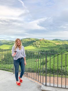 a woman standing on top of a hill next to a metal fence and looking at the camera