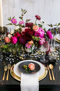 the table is set with black and gold plates, silverware, and pink flowers