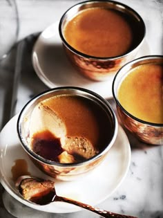 three cups filled with liquid sitting on top of a white plate next to spoons