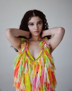 a woman in a colorful dress posing for the camera with her arms behind her head