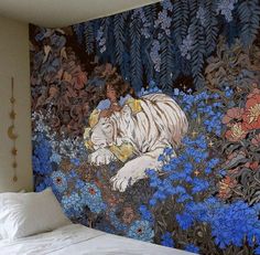 a bed with a white tiger laying on it's side in front of a wall mural