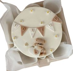 a teddy bear sitting on top of a white cake in a box with bunting